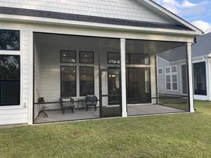 Screened back porch with black-framed screen panels, white columns, gray deck floor, and white vinyl siding