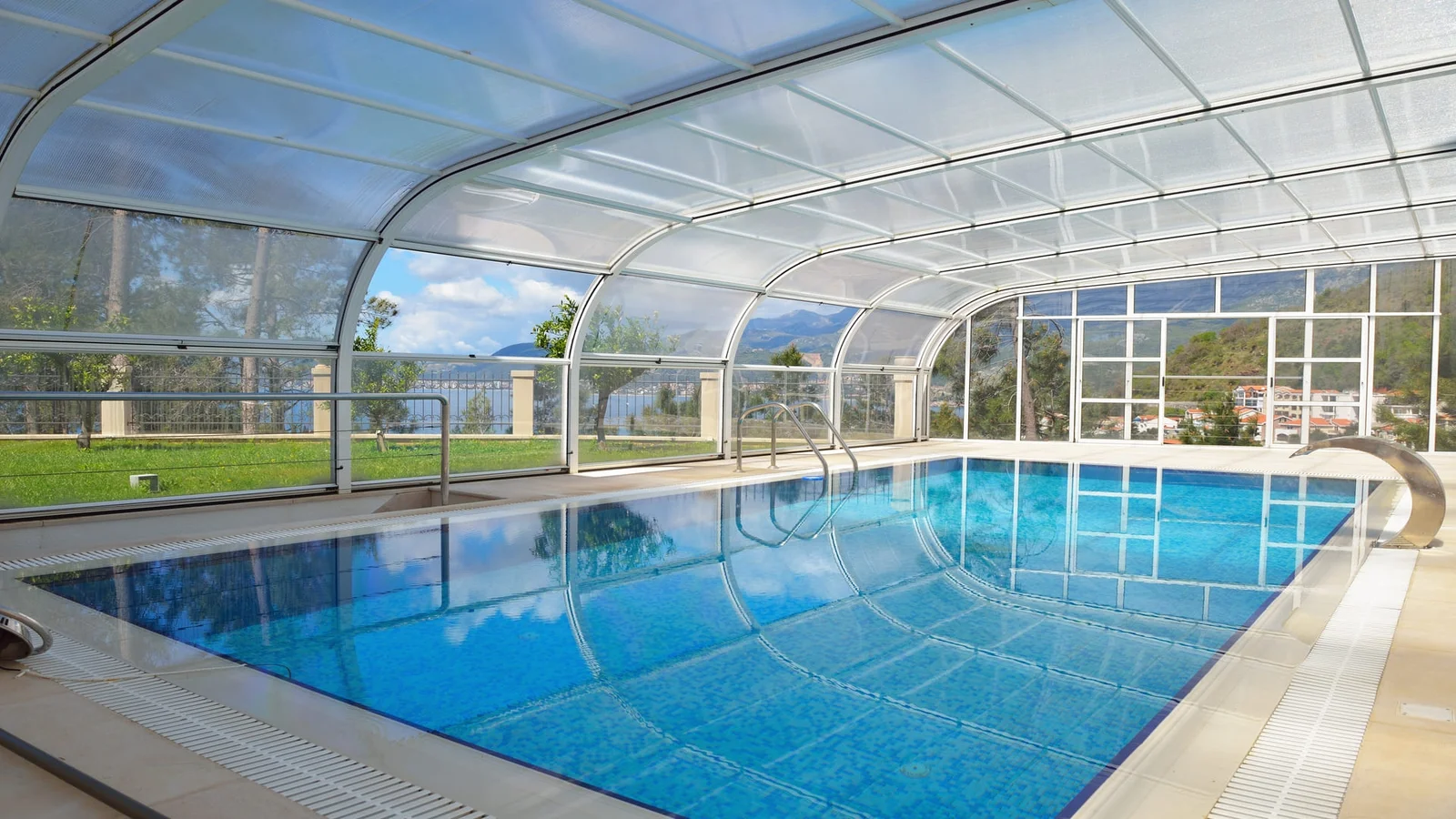 Arched pool enclosure with polycarbonate roof, aluminum framing, glass side panels, and stainless steel pool ladder