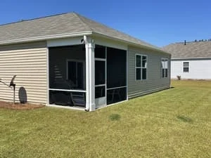 Screened back porch with white framing, dark gray screen panels, and beige vinyl siding on a single-story home