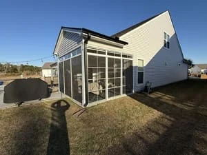 Rear view of a screened porch enclosure with aluminum-framed screen panels and a gable roof attached to a vinyl-sided home