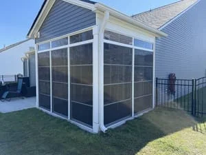 White-framed screened porch enclosure with dark mesh panels and transom windows beside gray siding