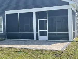 White-framed screened porch with dark mesh screen panels and screen door over a gray paver patio