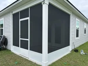 White-framed screened porch with dark charcoal mesh panels, white screen door, and white corner post beside vinyl siding