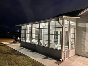 Enclosed back porch with gray base wall, white-framed glass and screen panels, and concrete patio at dusk
