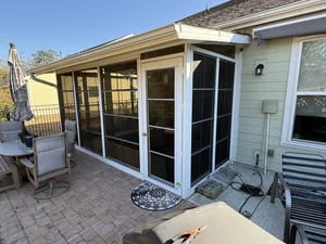 White-framed screen enclosure with French-style screen door on a paver patio under an extended roof